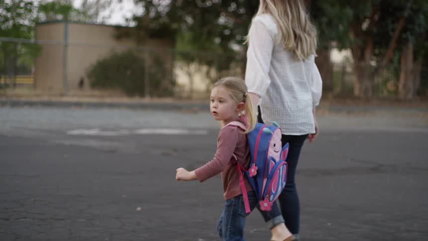 Little girl wearing a backpack with her mother holding her hand walking through a lot