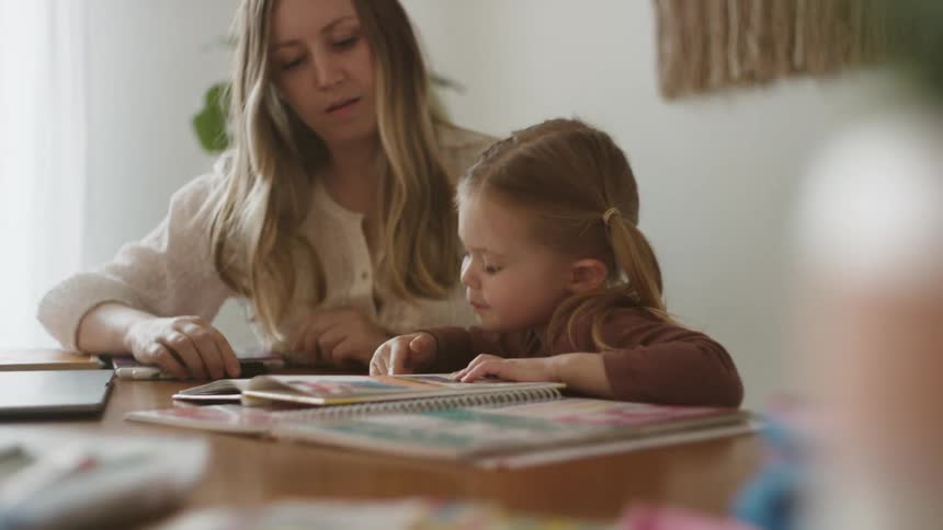 A woman and daughter sit at a table reading a book together