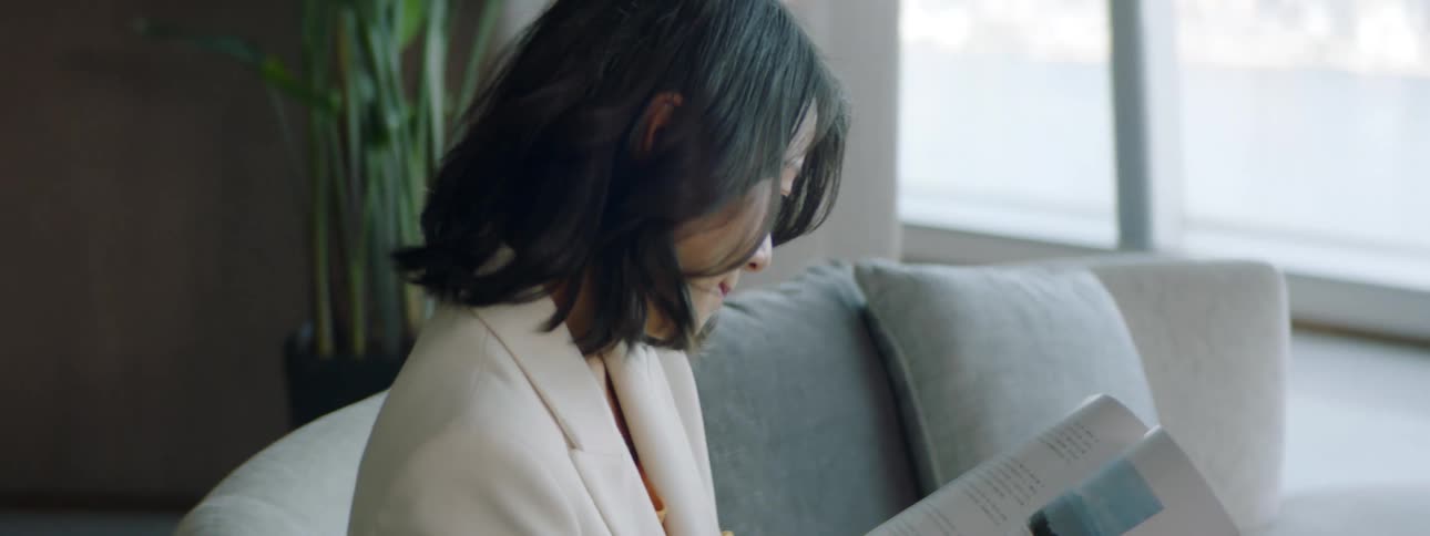 Asian businesswoman wearing a white blazer jacket sits on the sofa and reads a magazine in the lobby room