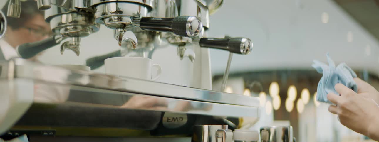 Person is reflected in coffee machine as they prepare coffee in shop