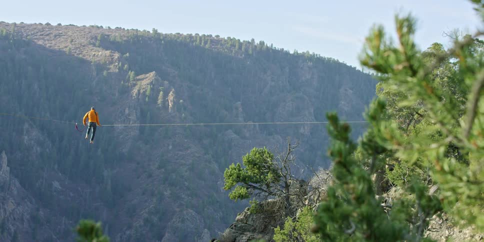 Person sitting on a high wire suspended above a large canyon