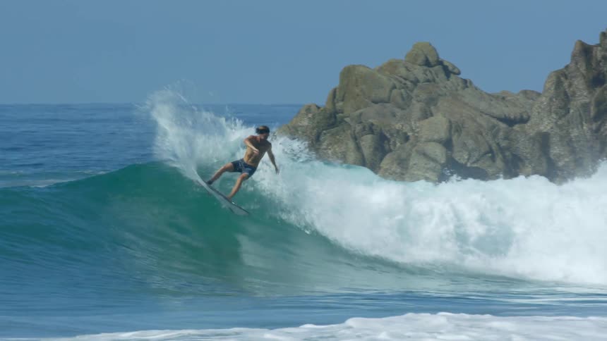 Male surfer rides a big wave with rock formations nearby
