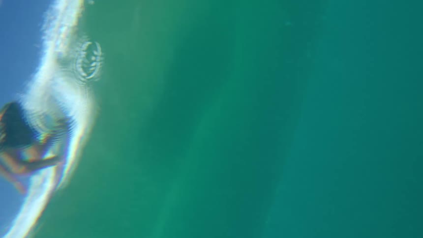 Man rides a wave on a surfboard seen from underwater