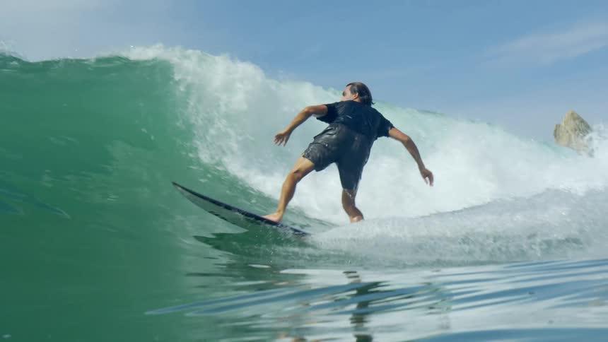 Male surfer with a black shirt and swimming shorts rides a wave on a purple surfboard