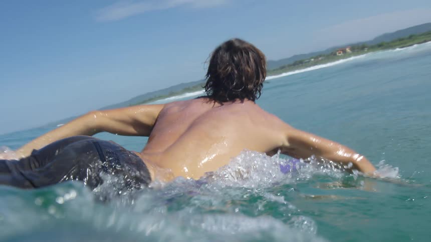 Young fit surfer rides a wave over a purple surfboard near the beach on the tropic