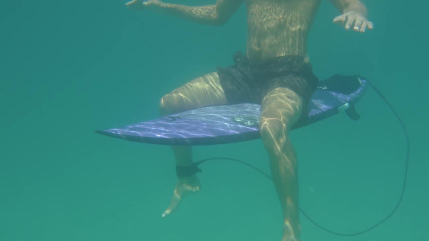 A man sits on a purple surfboard underwater with his head over the waters surface