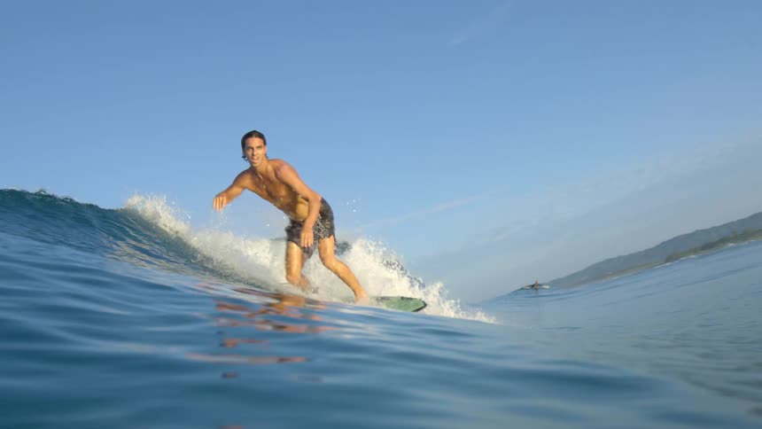 A young man paddles out onto a wave and stands up on his surfboard