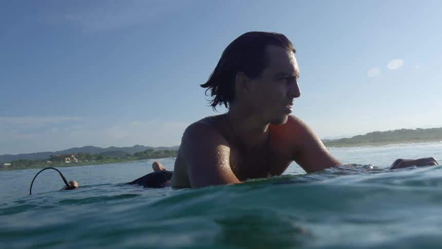 Male surfer lies on the surfboard in the sea water