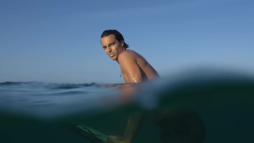 Man holds surfboard underwater with his upper torso above water and looks around