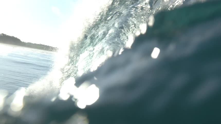 Splashing ocean wave rolls in on a clear day with coastline in the distant background