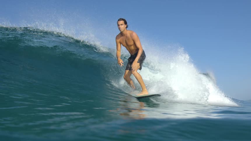 A man catches a wave and stands up on his surfboard to ride it