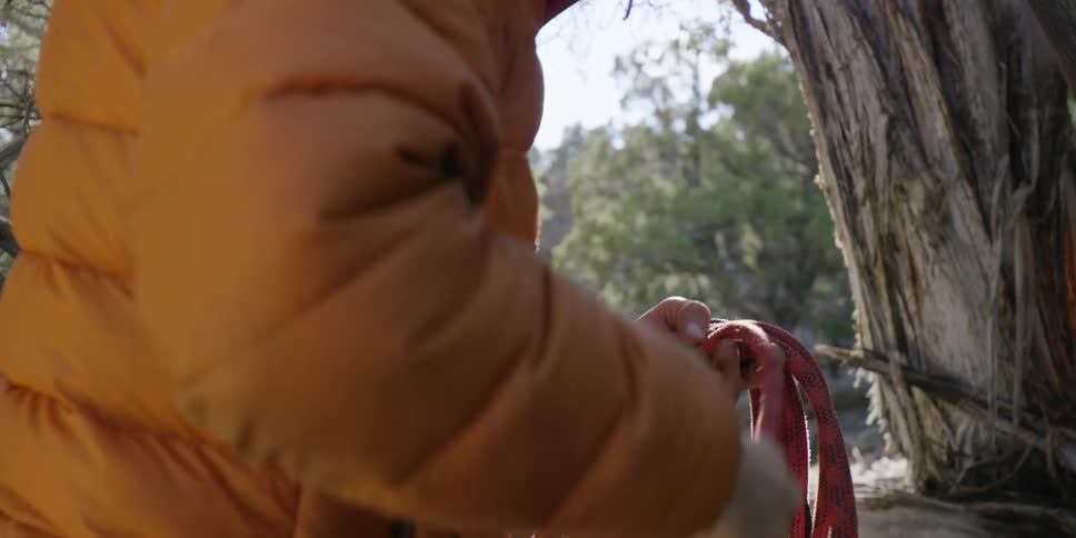 A man in a yellow jacket coils a rope