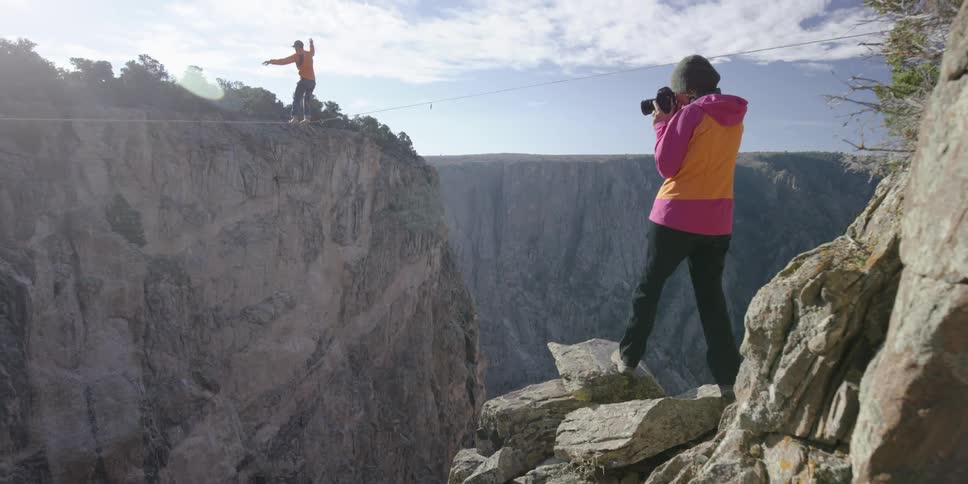 A man walking a tightrope across a canyon as a woman photographs him