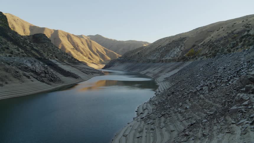 A mountain reservoir starts to run dry as the rocky shoreline grows larger and larger