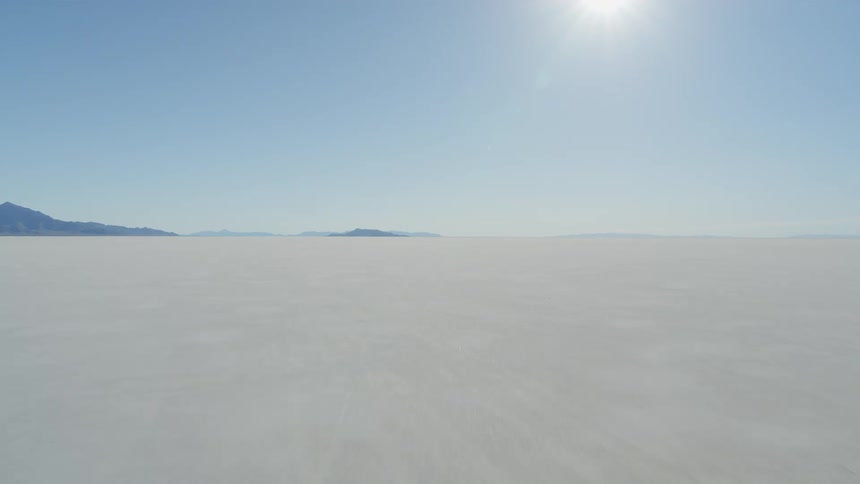 Low pullback over a vast desert of white salt as the hot sun shines down from above