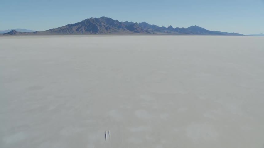 Tilt up reveal of hot and dry salt flats with craggy mountains in the distance