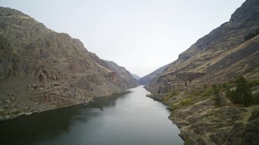 A calm river runs along the bottom of a mountain gorge at dawn