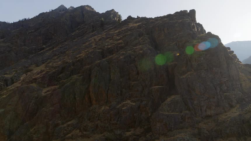 Orbit around the backlit ridge of a tall and rugged mountainside at sunrise