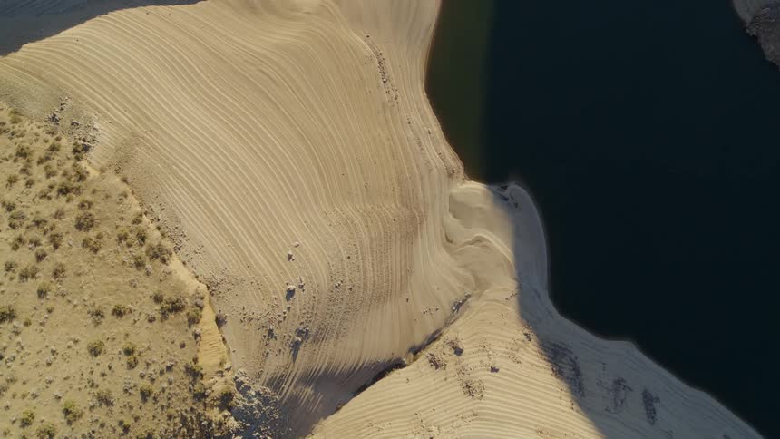 Aerial top down view of the striations along a receding riverbank in a desert canyon