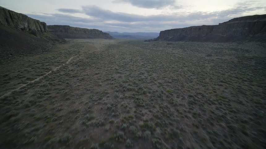 Tilt up reveal of a dry and arid flat valley floor surrounded by tall rocky cliffs