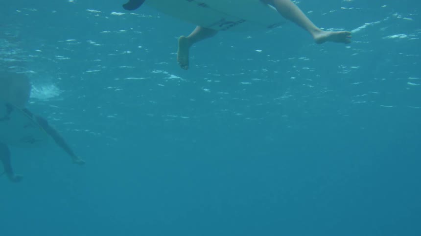 From underwater two surfers are seen sitting on their boards while kicking their legs