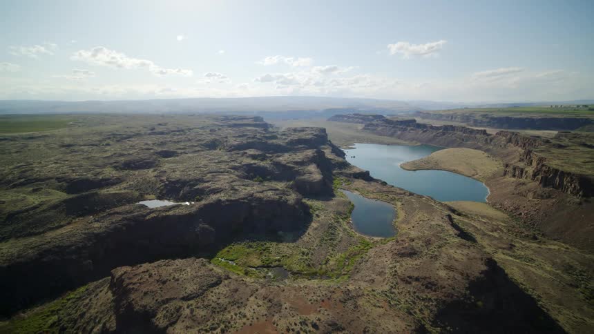 Traverse above rugged scablands with rocky cliffs and multiple ponds of water