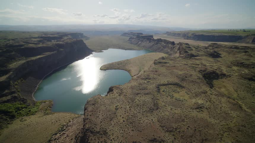 Tilt up reveal of tall rocky cliffs surrounding a deep canyon lake