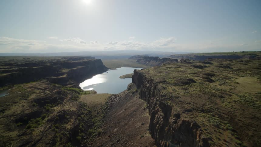 Skimming low above the edge of a rugged cliff to reveal a beautiful canyon landscape and deep water lake