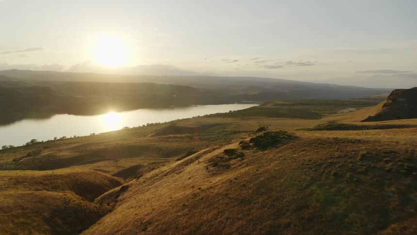 Descending along sun kissed hills toward a beautiful river valley as the sun sets in the distance