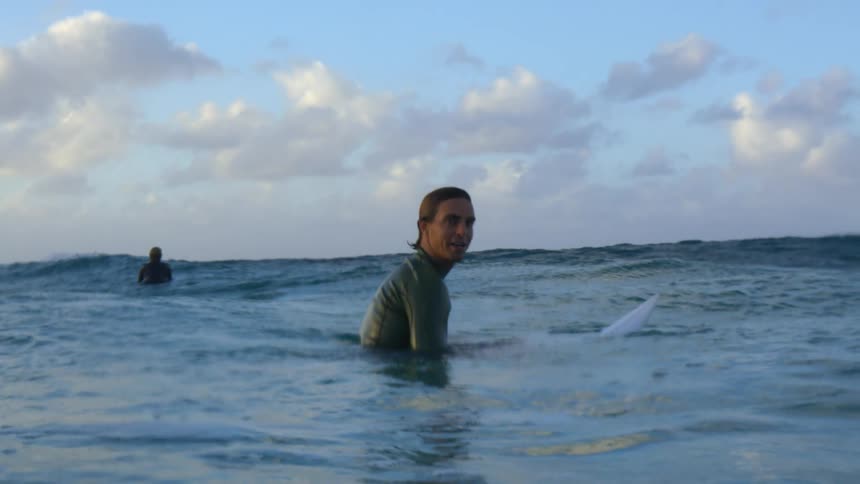 Surfer wearing a wet suit floating over a surfboard in the ocean