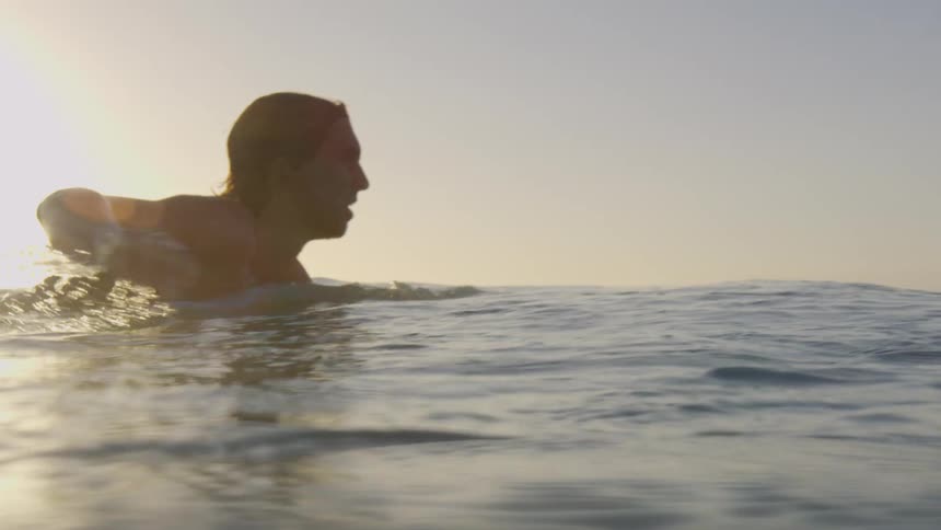A man in the ocean paddles his surfboard out