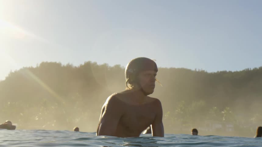 A man is in a body of water with other people behind him in the water with sunlight streaming down