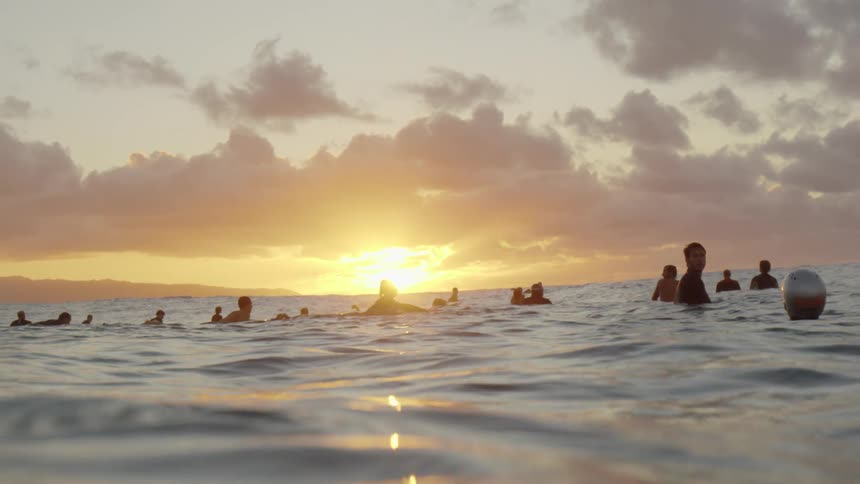 Surfers wait on boards in water as sun rises on horizon turning sky red
