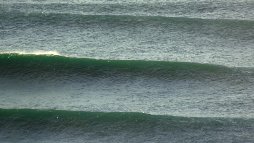 Wide shot of the ocean with three waves visible