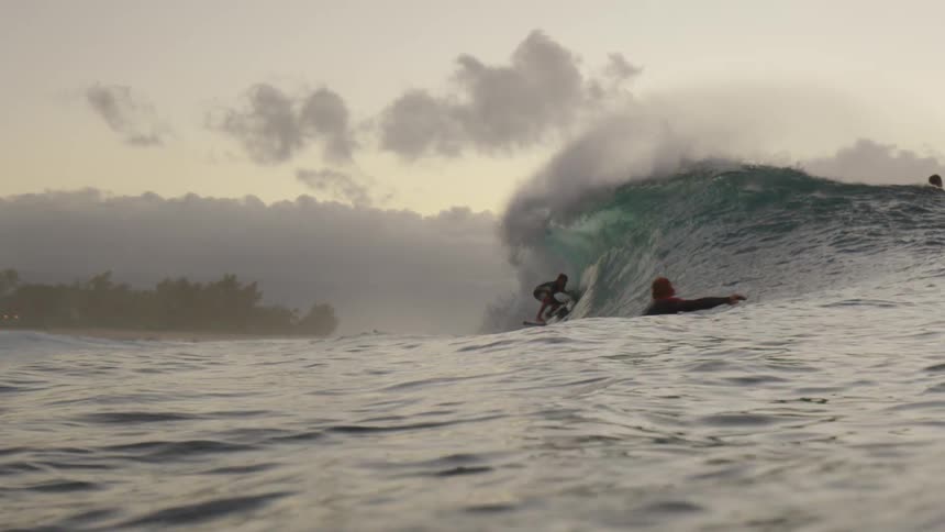 Male surfer rides on a wave on a surfboard on a cloudy day at dusk