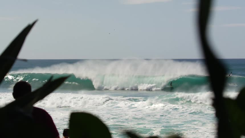 People are surfing in the ocean as other people watch from the shore