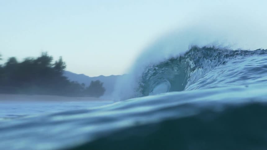A close up of a wave cresting with a shoreline in the background