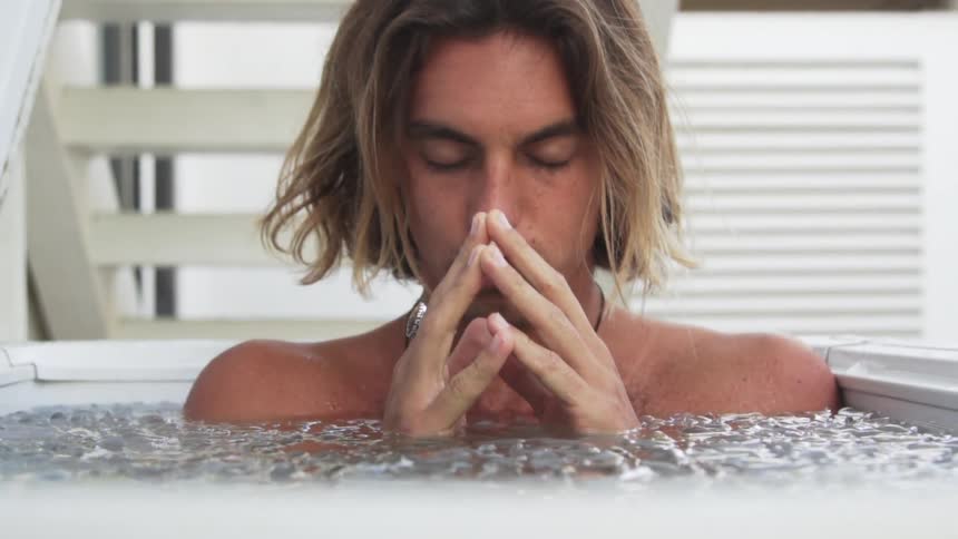Man sits in tub of ice water with eyes closed and fingers templed in front of white steps