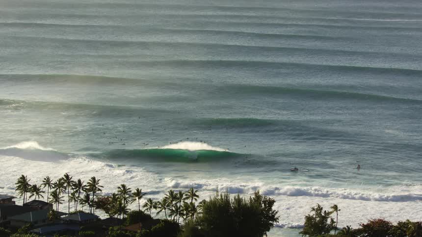 Multiple waves wash up upon a coastal beach lined with trees and cottages