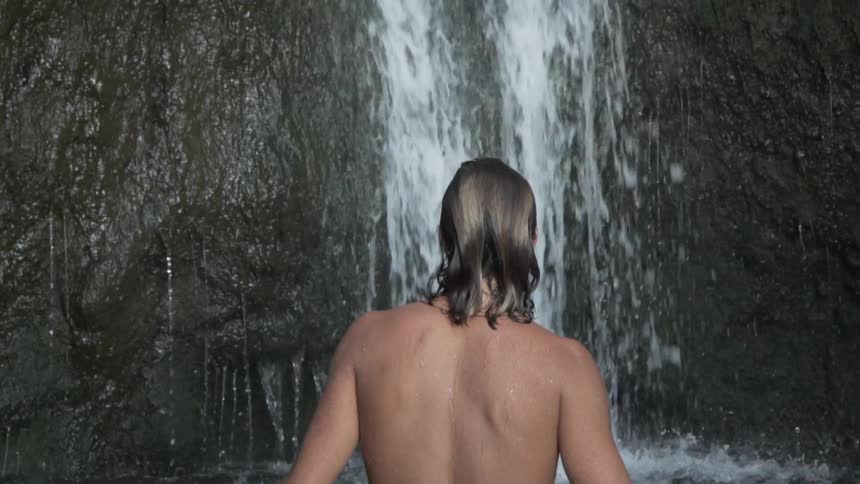 Man with out a shirt on walks to a waterfall