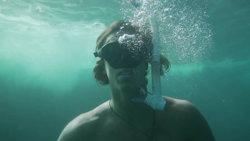 A snorkeler exhales water from his mouth while floating just below the surface of the ocean during the day