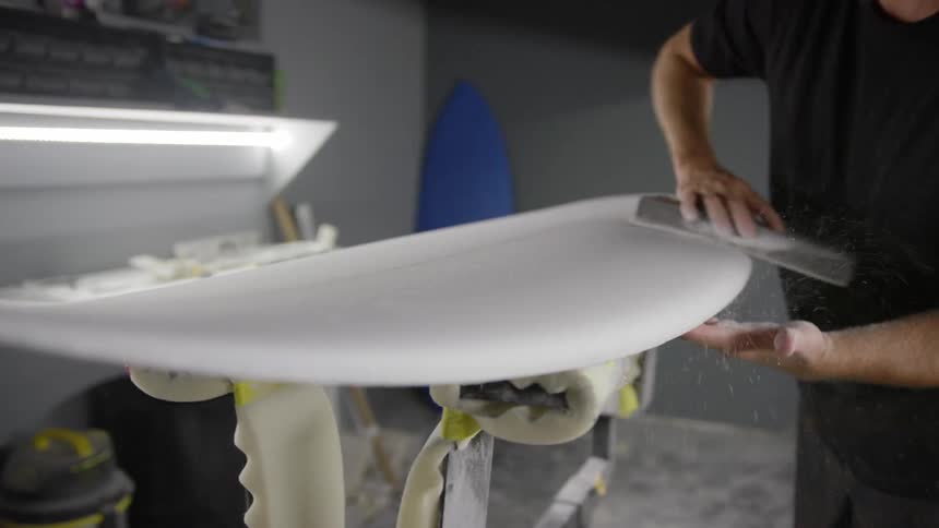 Man standing the surface of a surfboard in side a workshop