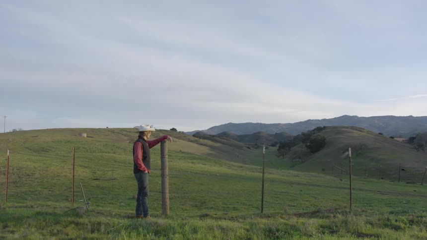 Young cowboy reclining in a wooden post in the grassland next to the hills
