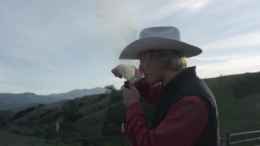 A man takes a puff from his pipe while igniting the contents with his lighter as he stands in the hills in the countryside during the day