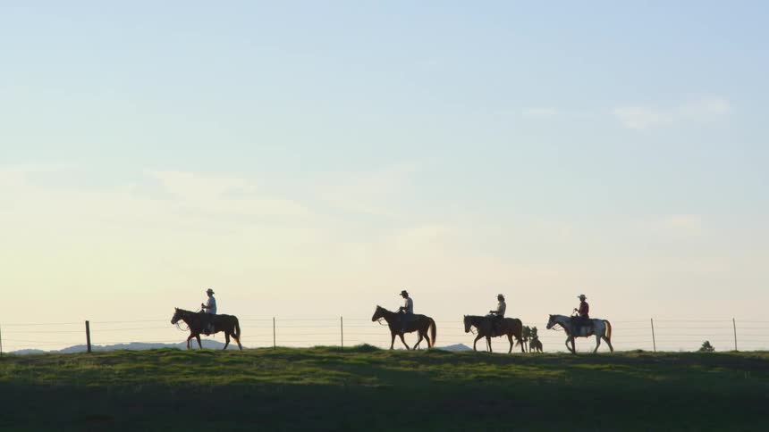 People riding horses on a grassy field with a fence the sky and clouds in the background