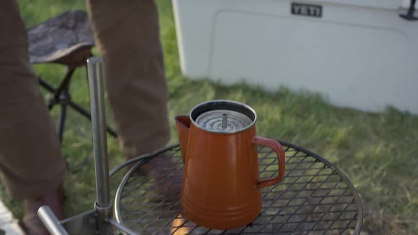 A camper places the plunger on a coffee press that hes heating over a fire