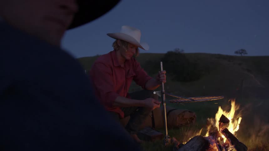 A man sets a grill up over a fire outdoors