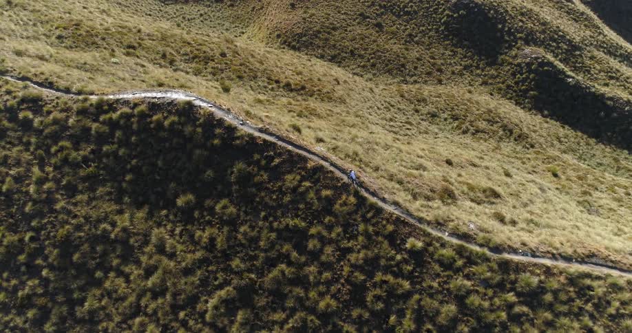 An aerial view of a hilltop with a person walking on a trail with a bike during the day