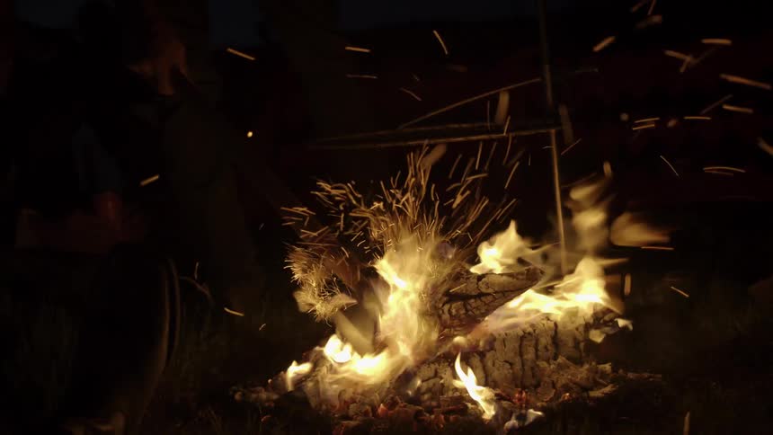 A camper uses an axe to move a piece of burning wood in a campfire