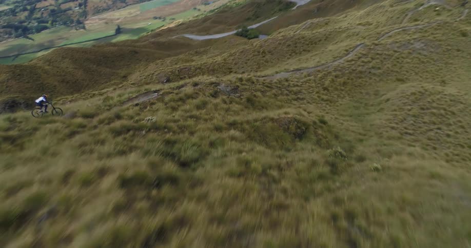 Person rides bike very fast down a steep hilly path with trees mountains and valleys in the distance